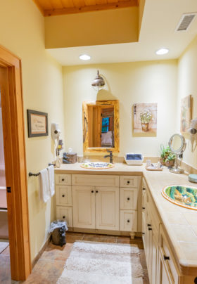Large bathroom with 2 hand painted sinks. Two wooden mirrors with sconces over the top. There are 2 hairdryers on the wall surrounded by pictures. Rug is on the heated tile floors. Tub and shower combination is on left hand side of room. Large L shaped vanity area.