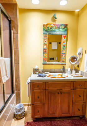 Rainbow trout bathroom.. shower/bath combo with glass doors. Yellow walls with mirror, hair dryer and towel bar over wood chest with painted sink bowl. Water Closet is on the right side of the room