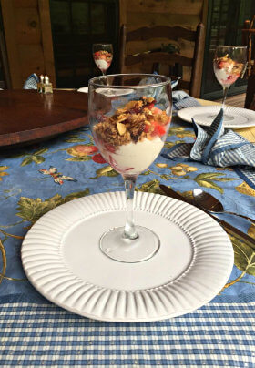 white plate with wine glass filled with yogurt ,fruit and granola