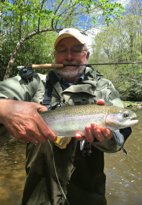 Man holding rainbow trout standing in the river